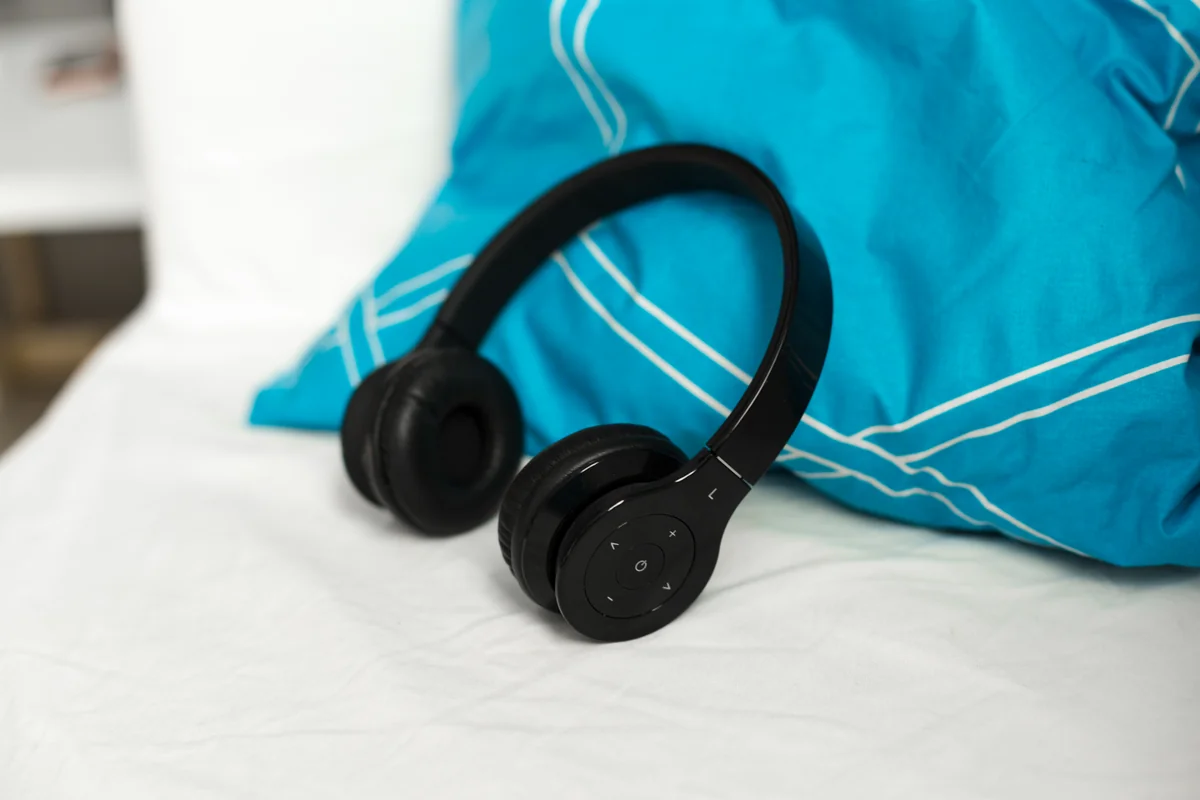 Casque audio noir posé sur un lit près d'un coussin bleu