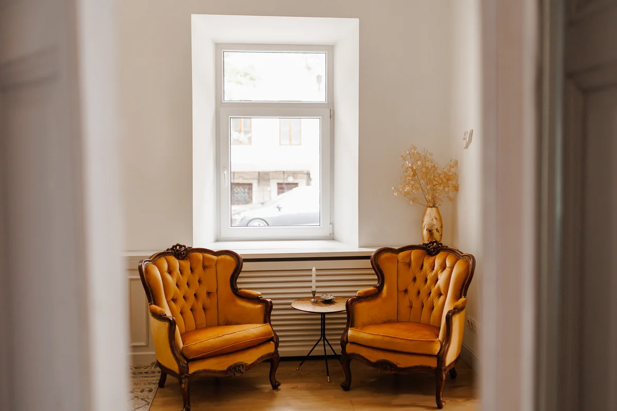 Deux fauteuils anciens moutarde de part et d'autre d'une fenêtre, dans un intérieur calme