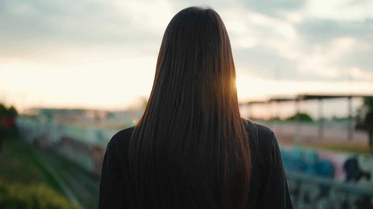 Femme aux longs cheveux bruns vue de dos face au soleil couchant