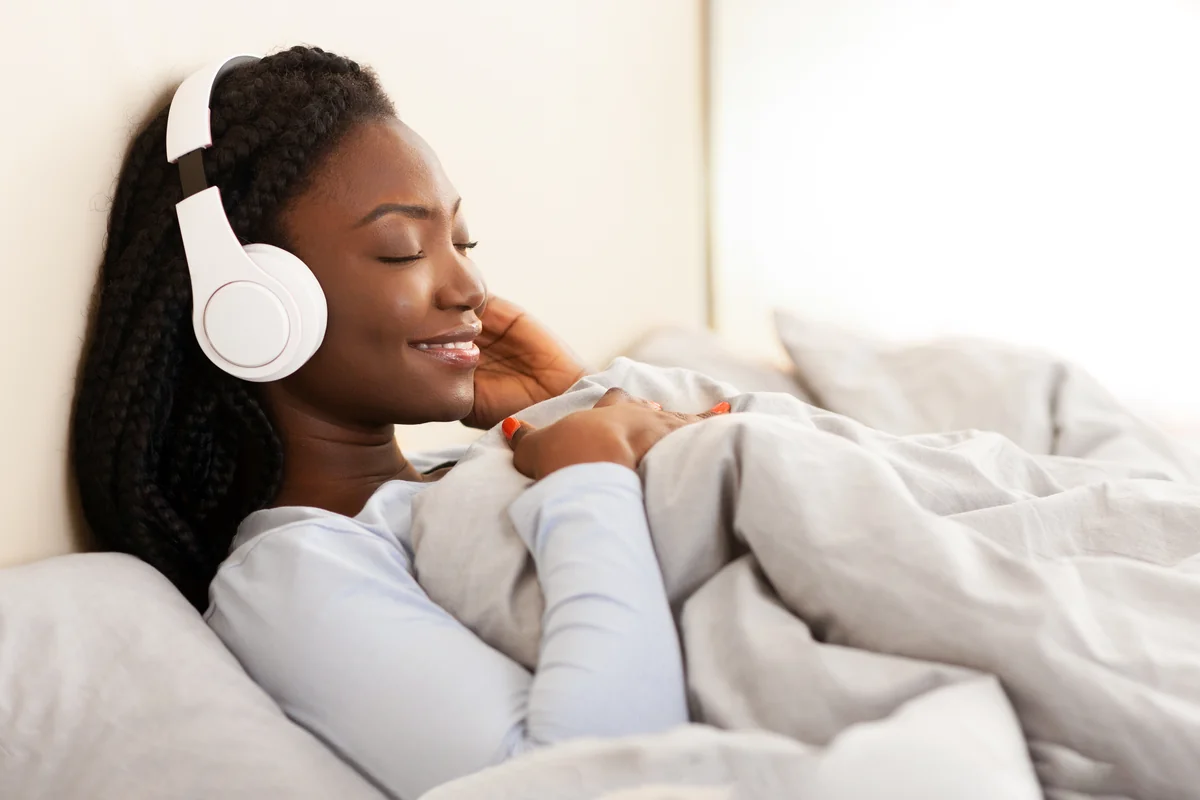 Femme souriante écoutant de la musique au casque, allongée dans son lit