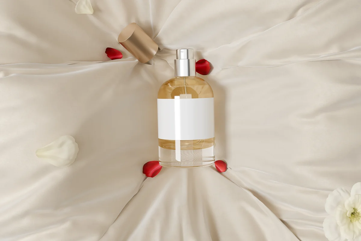 Flacon de parfum posé sur un drap de soie blanc parsemé de pétales rouges