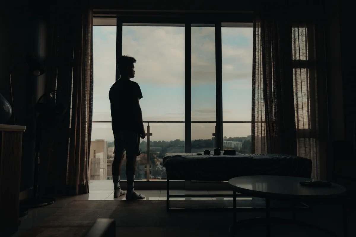Silhouette d'un homme debout devant une baie vitrée dans un appartement sombre