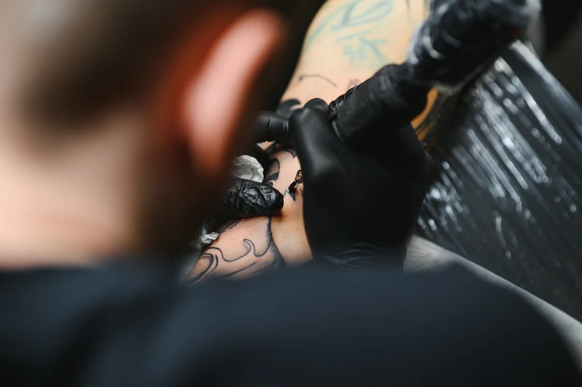 Tatoueur aux gants noirs travaillant sur un bras